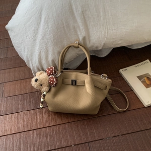 Close-up of khaki lychee grain bucket bag with cute plush bear charm on wooden floor