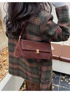 Dettaglio di una borsa baguette vintage in camoscio marrone con chiusura dorata su un blazer