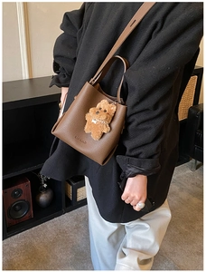 Detailed texture of a brown pebbled leather bucket bag with a cute bear charm pendant