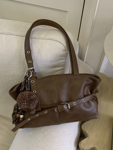Vintage dark brown tote bag with metal eyelet straps and charm on white sofa