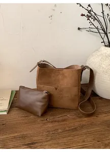 Détail du sac seau en daim marron et sa pochette en cuir sur une surface en bois