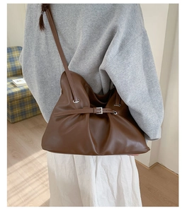 Detail of dark brown pleated tote bag with metal buckle strap and soft leather texture