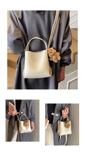 Detail of beige lychee leather bucket bag featuring a plush bear charm and brand logo