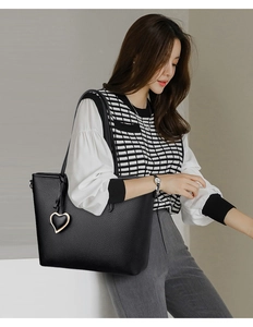 Detail of black pebbled leather tote bag featuring a golden heart-shaped metal charm