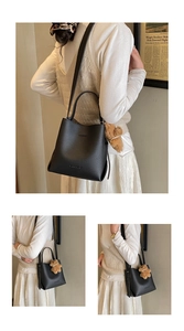 Black litchi grain bucket bag detail with BAGUMRO logo and brown plush bear charm