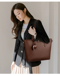 Detail of a brown tote bag with heart pendant worn by a model in a black blazer