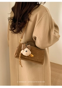 Brown retro suede crossbody bag with gold lock and plush pendant on beige wool coat