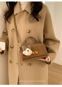 Close-up of retro caramel brown crossbody bag with gold twist lock and plush bear charm