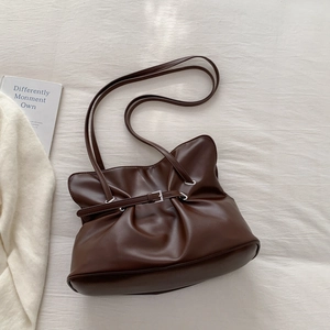 Detailed close-up of dark brown pleated leather bag with silver buckle on white fabric