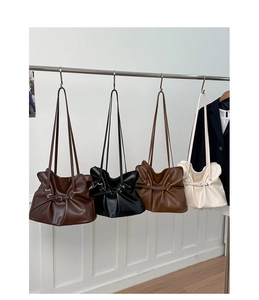 Collection of pleated tote bags in dark brown, black, caramel and cream hanging on a rack