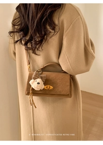 Detailed close-up of brown suede crossbody bag with gold lock and plush bear charm