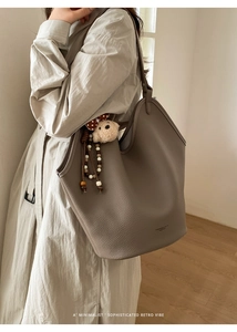 Détail du sac cabas en cuir taupe avec un charm ours en peluche et décor perlé