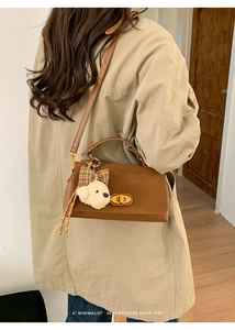 Detail of brown faux suede crossbody bag with gold lock and plush bear charm on model