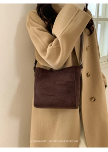 Détail du sac seau en daim marron foncé avec poche en V sur un manteau de chameau
