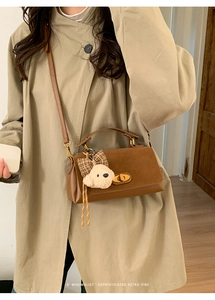 Detail of retro brown leather crossbody bag with teddy bear pendant on beige coat