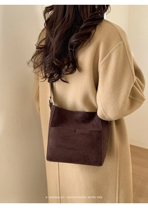 Vue détaillée du sac seau en daim marron foncé porté avec un manteau camel de style rétro