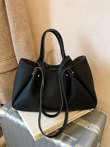 Minimalist black lychee texture leather tote bag with silver studs on a silver suitcase