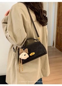 Detail of minimalist black crossbody bag with a cute plush dog charm and gold twist lock