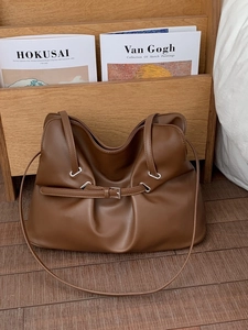 Caramel brown pleated tote bag with silver buckle on a wooden background