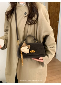 Detail of retro suede handbag featuring gold twist lock and cute plush bear charm