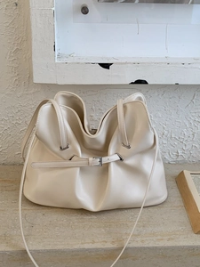 Cream pleated tote bag with cloud silhouette and slender shoulder strap on stone base
