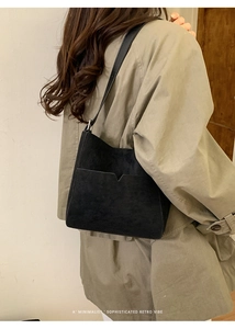 Détail d'un sac hobo rétro en daim noir avec poche en V sur un manteau kaki
