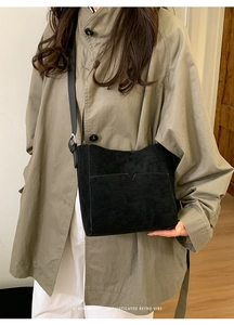 Détail d'un sac seau en daim noir avec poche en V sur un trench-coat de couleur kaki