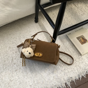 Detail of vintage brown suede crossbody bag featuring gold twist lock and cute teddy charm