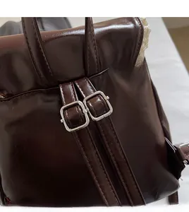 Detail of adjustable metal buckle and stitching on dark brown faux leather backpack strap