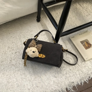 Detail of dark brown suede handbag featuring a gold twist lock and a cute bear charm
