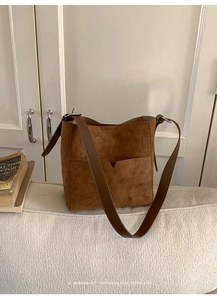 Gros plan d'un sac seau en daim marron avec poche avant en V et bandoulière en cuir