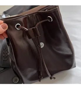 Detailed view of dark brown glossy leather bucket bag with drawstring and magnetic closure