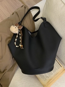 Sac seau rétro en cuir noir avec breloque en peluche sur canapé beige, style décontracté
