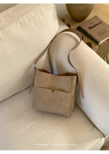 Détail d'un sac seau en daim marron avec poche en V sur un canapé minimaliste