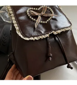 Detail of coffee PU leather backpack featuring lace edges and a pearl heart decoration