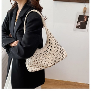 Detail of cream hobo bag with silver metallic studs worn with a black blazer