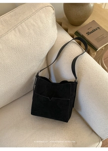 Détail d'un sac seau noir en daim avec poche en V sur un canapé crème texturé