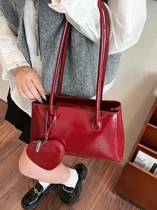 Glossy red faux leather tote bag with heart charm shown in a warm indoor setting