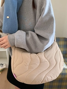 Beige quilted crescent crossbody bag with wave texture and purple accent tag