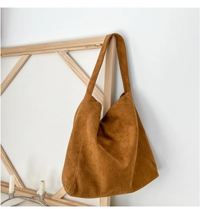 Vue détaillée du sac hobo en daim marron suspendu sur un cadre en bois épuré