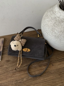 Vintage dark grey suede handbag with golden swivel lock and plush bear charm on wood