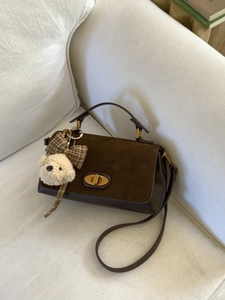 Retro dark brown suede handbag with golden twist lock and plush puppy charm on a soft sofa