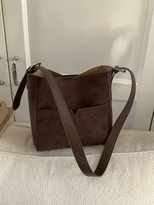 Deep brown minimalist bucket bag with front pocket and adjustable shoulder strap
