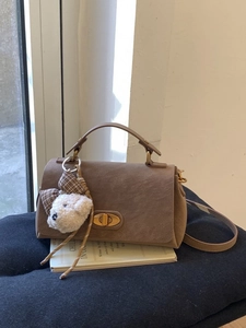 Vintage brown suede handbag with metal lock and teddy bear charm on a book