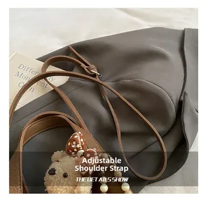 Détail d'un sac en cuir marron montrant la bandoulière réglable et l'ourson décoratif