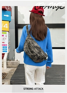 Detail view of camouflage crossbody chest bag on model wearing a blue sweater and white pants