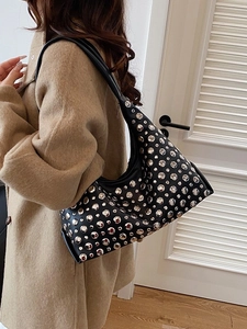 Modern black leather hobo bag with silver metallic studs worn with a beige coat