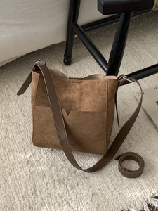 Brown suede bucket bag with long shoulder strap displayed on a textured rug