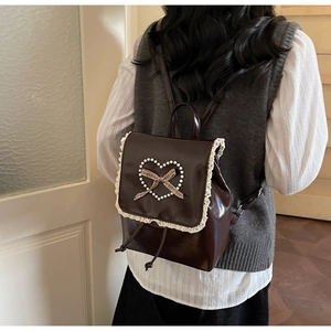 Détail du sac à dos en cuir marron avec bordure en dentelle, cœur en perles et nœud à carreaux