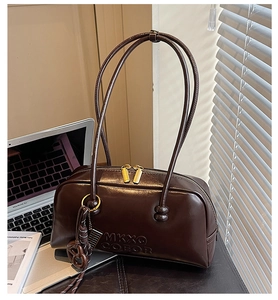 Detail of dark brown matte leather pillow bag with gold zippers in a cozy office setting